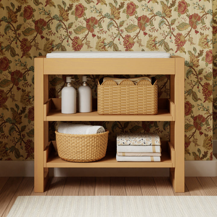 Front view of Namesake's Nantucket Changing Table stacked with items and changing pad in -- Color_Honey