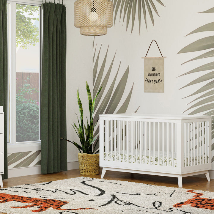 Babyletto's Scoot 3-in-1 Convertible Crib next to a window and plant  in -- Color_White