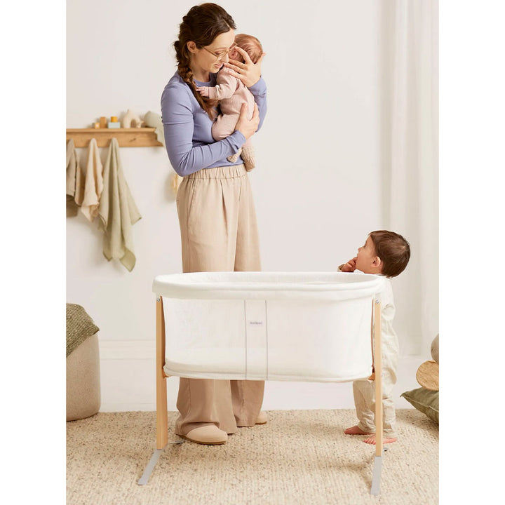 Toddler next to BABYBJÖRN Cradle looking up at mom and baby