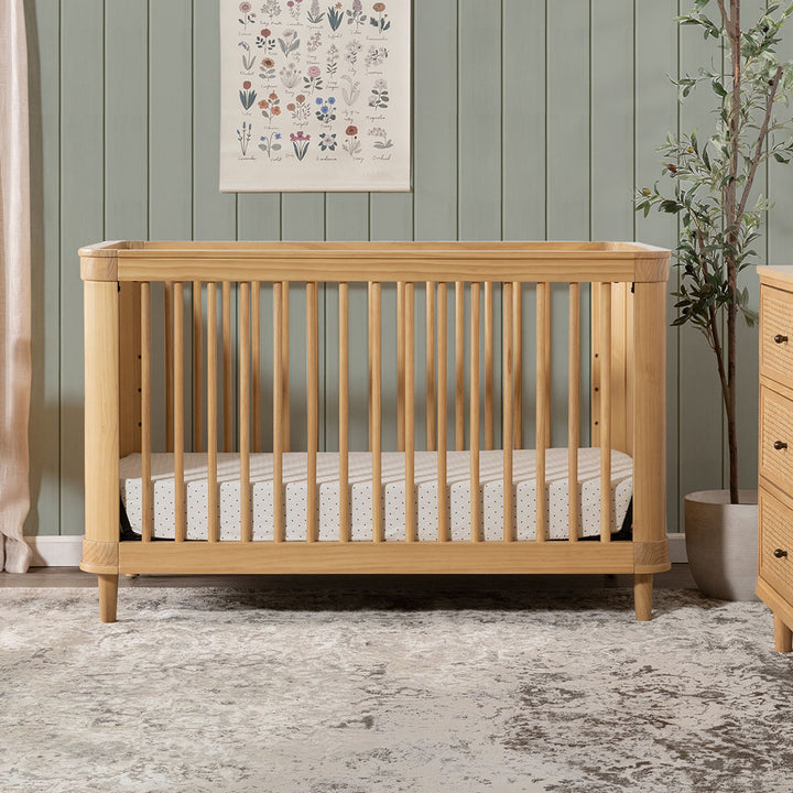 The Namesake Marin 3-in-1 Convertible Crib next to a plant in -- Color_Honey/Honey Cane