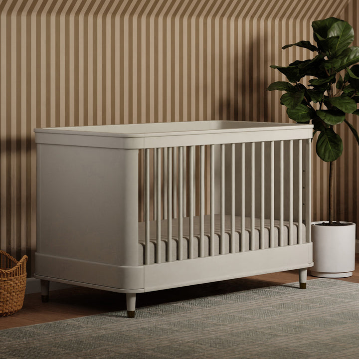 Namesake's Tanner 3-in-1 Convertible Crib next to a plant