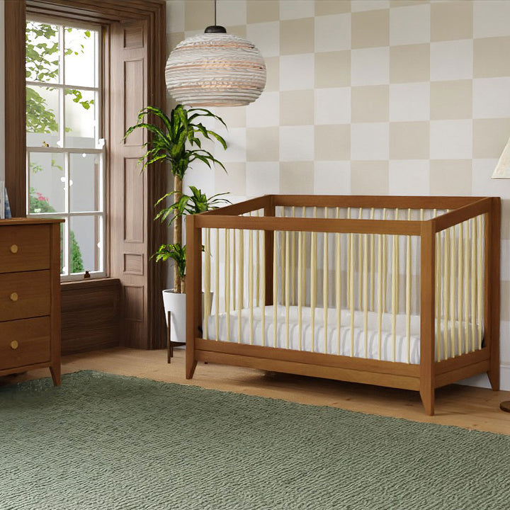 Babyletto's Sprout 4-in-1 Convertible Crib next to a plant and dresser in -- Color_Chestnut / Natural