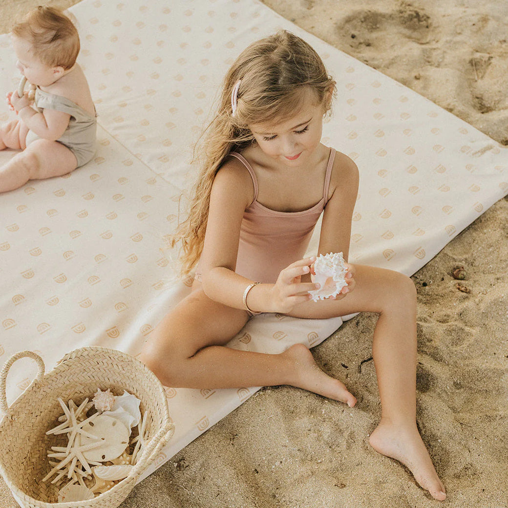 Toddler and baby sitting on the Toki Mats Vegan Leather Play Mat on the beach in -- Color_Rainbow Cream