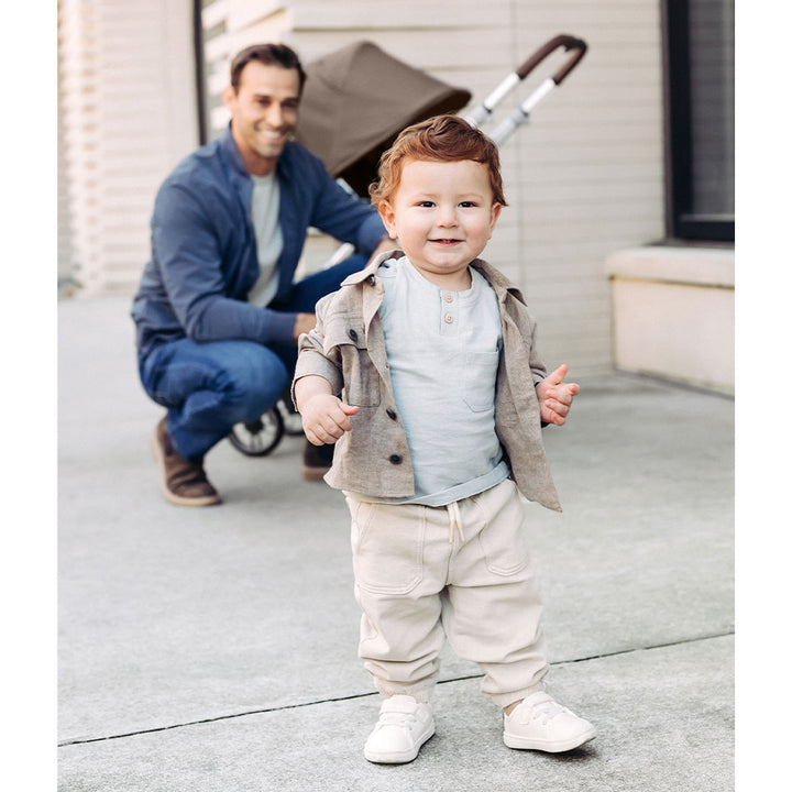 Baby walking in front of dad and UPPAbaby CRUZ V2 Travel System stroller in -- Color_Theo