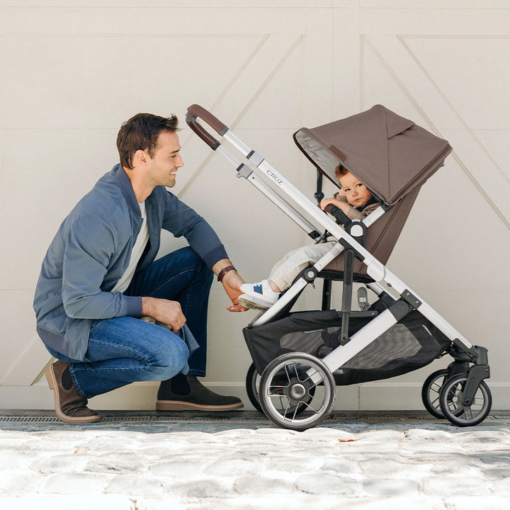 Dad looking at baby sitting in the reversed UPPAbaby CRUZ V2 Travel System stroller in -- Color_Theo