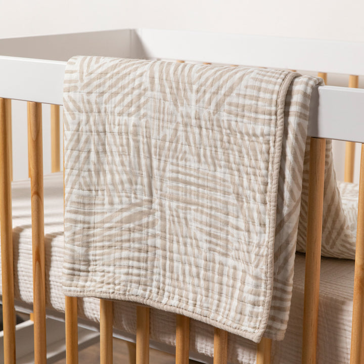 Babyletto's Quilt In 3-Layer GOTS Certified Organic Muslin Cotton over a crib rail in -- Color_Oat Stripe