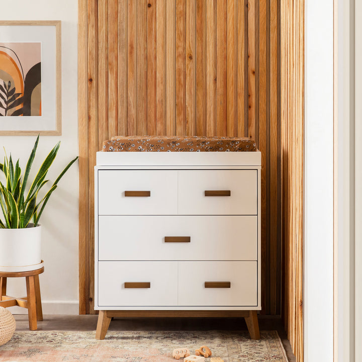 Front view Babyletto's Scoot 3-Drawer Changer Dresser next to a plant in -- Color_White/Natural Walnut