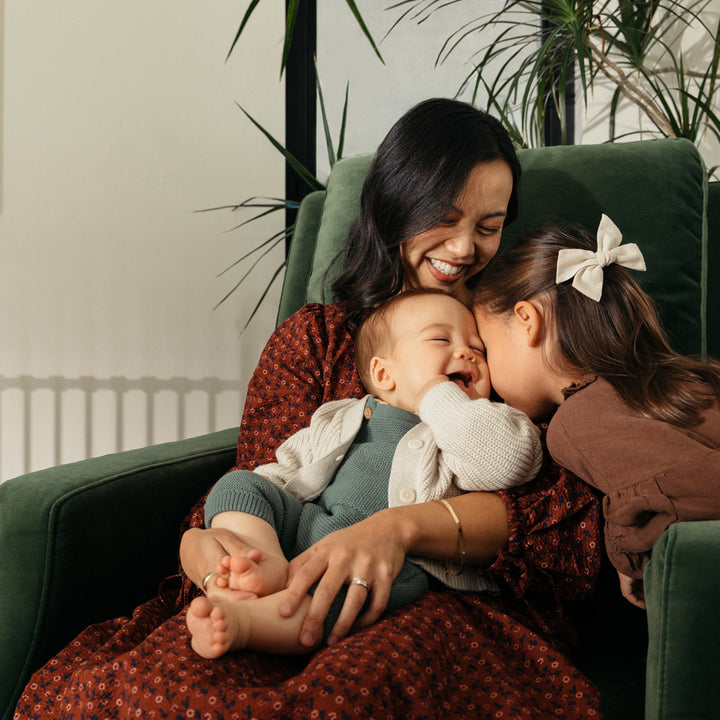 Mother with a baby and a toddler sitting in the Crewe Recliner & Swivel Glider in -- Color_Forest Green Velvet With Light Wood Base