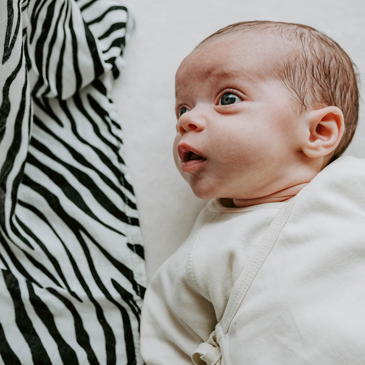 Baby lying down looking at the The Etta Loves Sensory Muslin in -- Color_Animal