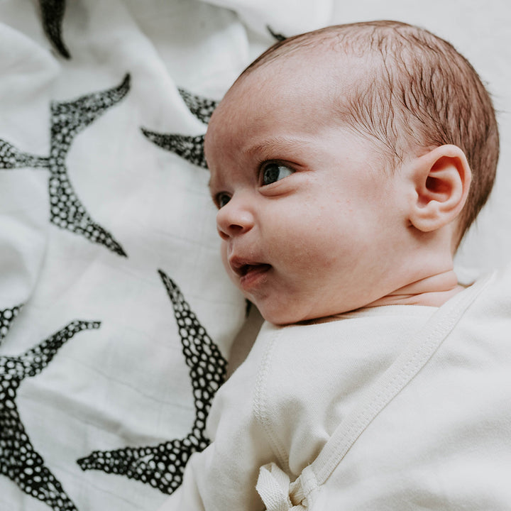 Baby lying down and looking at The Etta Loves Sensory Muslin in -- Color_Animal