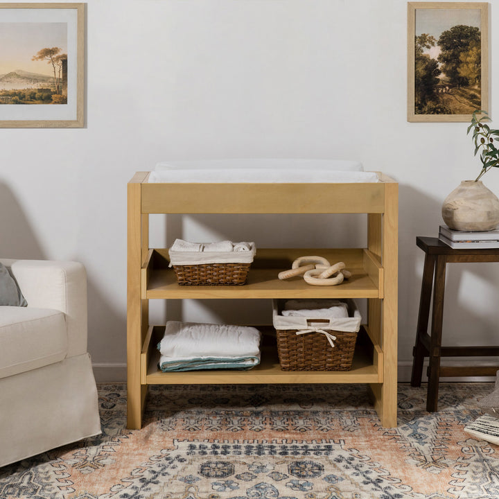 Front view of Namesake's Nantucket Changing Table next to a recliner  in -- Color_Honey