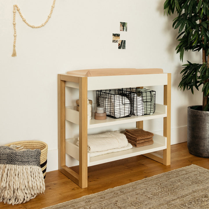 Namesake's Nantucket Changing Table next to a basket and plant  in -- Color_Warm White/Honey