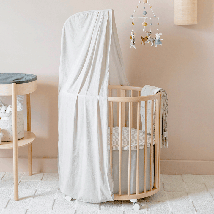 An empty crib equipped with a Stokke's  Sleepi V3 Mini Fitted Sheet By Pehr in -- Color_Stripes Away Pebbles