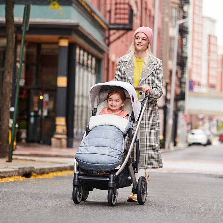 Mom pushing a baby down the street in the UPPAbaby Cruz V2 Stroller in -- Color_Gregory