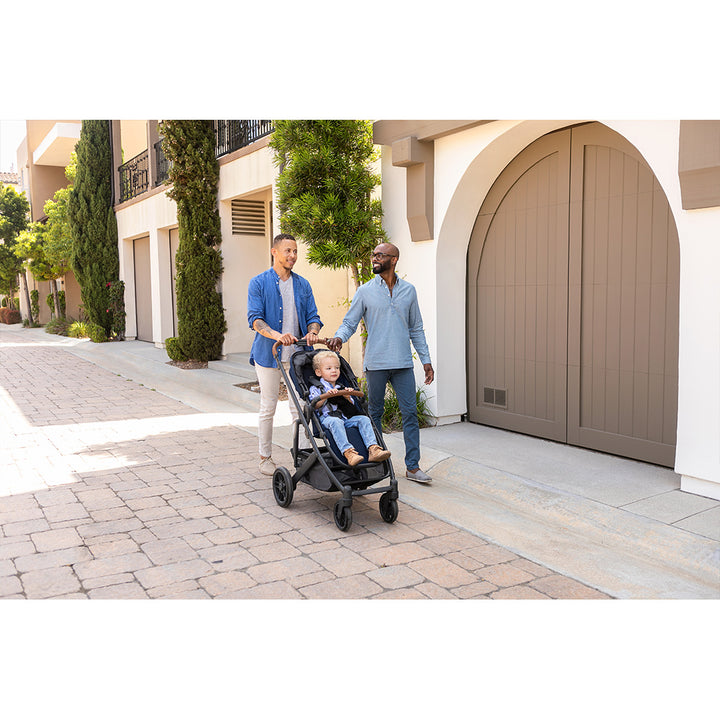 Two dads walking down the street pushing a toddler in the UPPAbaby CRUZ V2 Stroller in -- Color_Noa