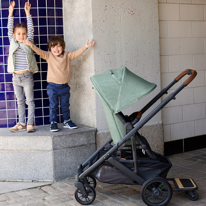 Two kids standing next to the UPPAbaby CRUZ V2 Stroller in -- Color_Gwen