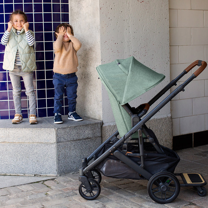 Two kids playing next to the UPPAbaby Cruz V2 Stroller in -- Color_Gwen