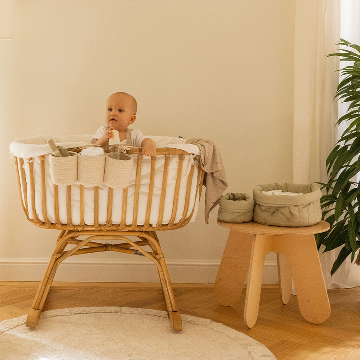 Lorena Canals Bambie Quilted Baskets next to a crib with baby  in -- Color_Olive