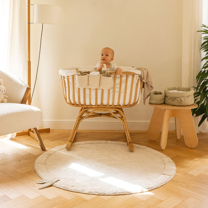 Lorena Canals Bamboo Leaf Washable Rug next to a crib with baby in it 