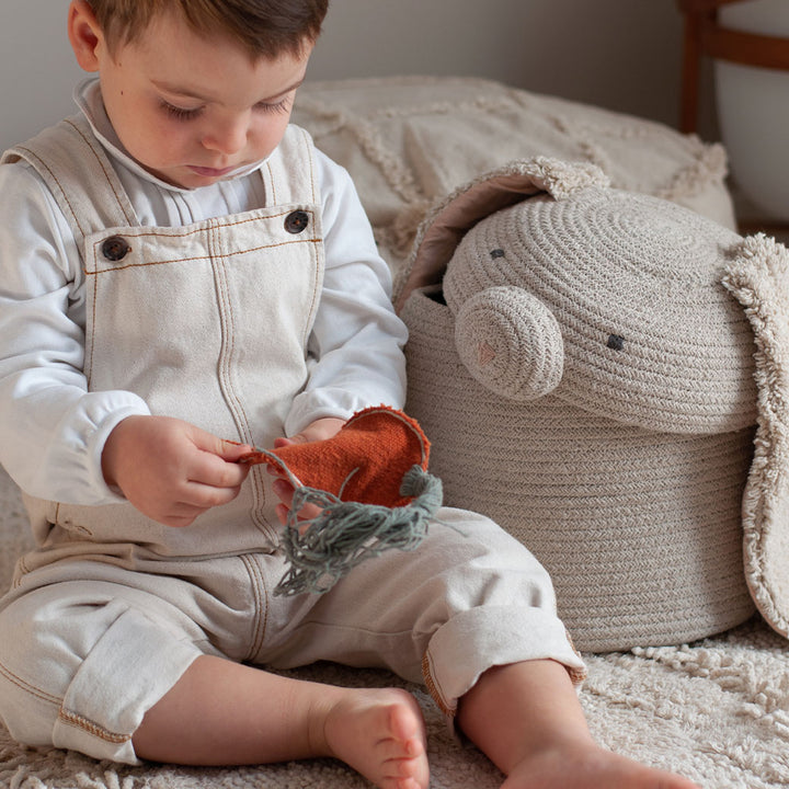 A child sitting next to Lorena Canals Rita the Rabbit Basket and playing with a toy